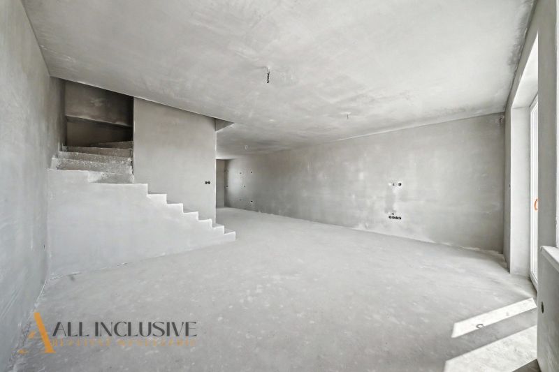 A spacious interior of an unfinished family house with a concrete staircase and bare walls.