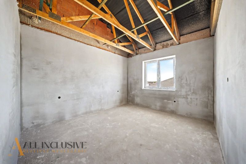 An unfinished room in a family house with a view of the roof beams and a window.