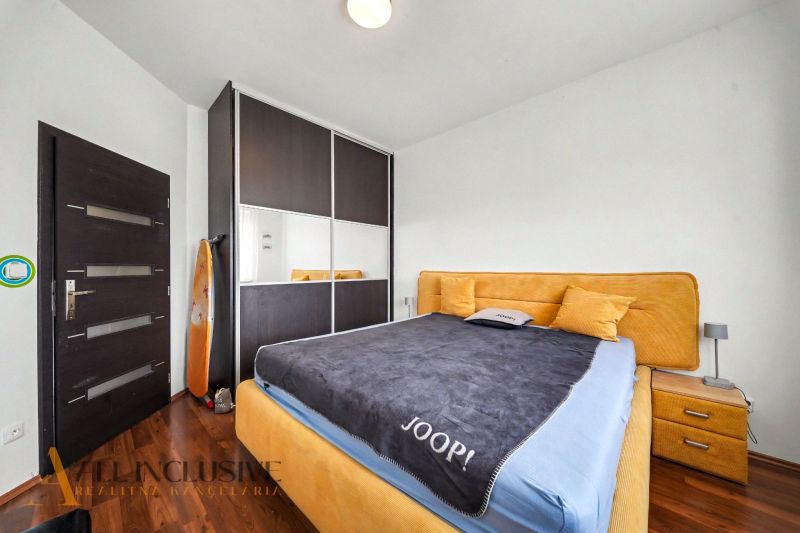 A bedroom in a family house with a bed, built-in wardrobe, and wooden decor flooring.
