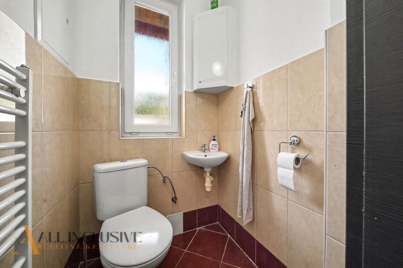 Bathroom with toilet and sink in a family house, beige tiles, white window.