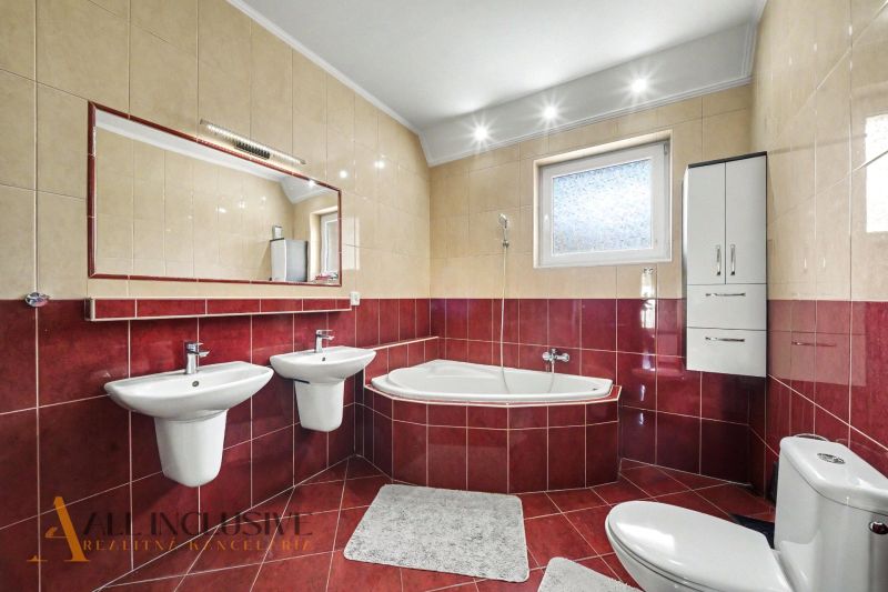 A bathroom in a family house with a corner bathtub and two sinks, red tiles.