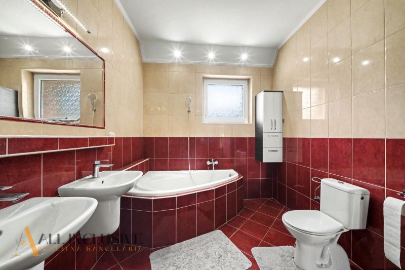A bathroom in a family house with a corner bathtub, red and beige tiles.