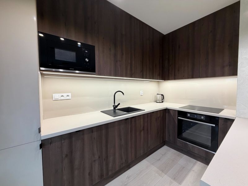 A kitchen in a 2-room apartment with dark cabinets and a wood-patterned floor.