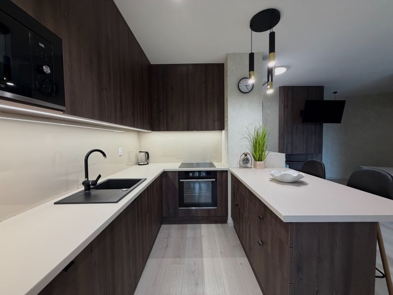 A kitchen in a 2-room apartment with dark furniture and a wooden decor floor.