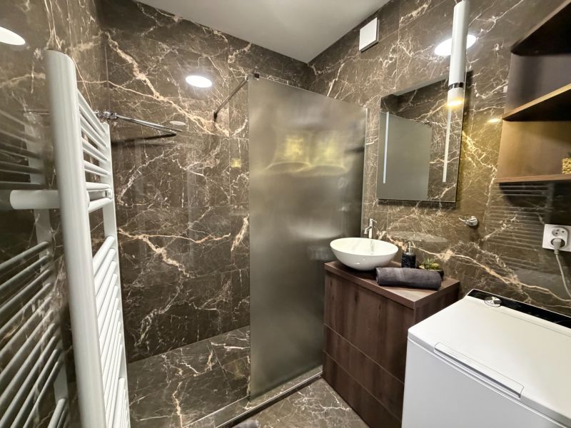 A bathroom with stone tiles, a shower corner, and a washing machine in a 2-room apartment.