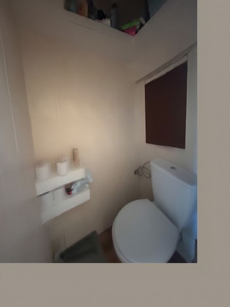 A bathroom in a 3-room apartment with a toilet, a shelf, and a blind on the window.