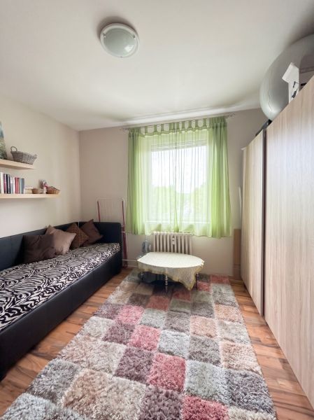 A room in a 3-room apartment with a sofa, shelves, a table, and a wooden decor floor.