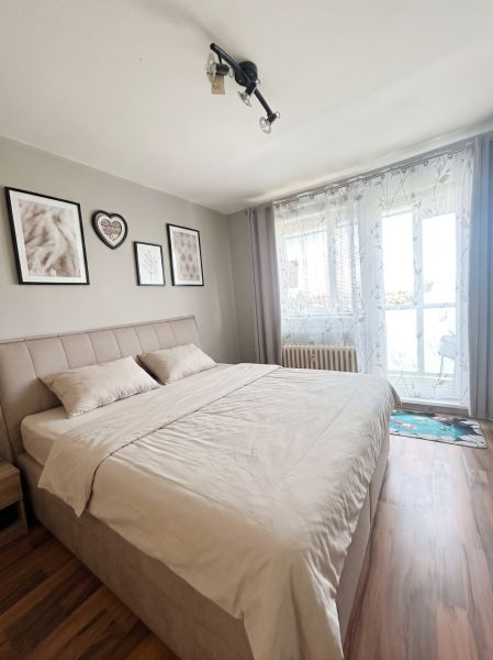 A bedroom in a three-room apartment with a wooden decor floor and balcony doors.