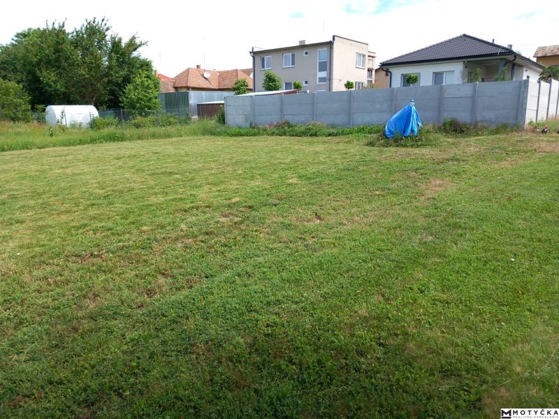 A grassy plot for living in Beladice, surrounded by a fence and family houses.