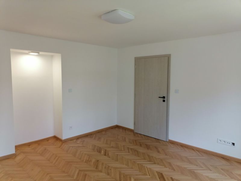 A bright room with wood-decor flooring and white walls in a two-room apartment.