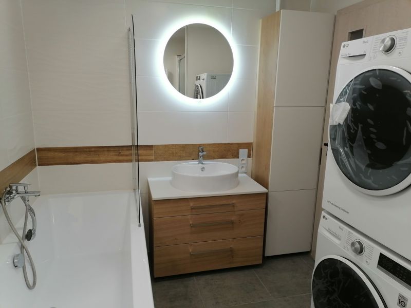 Bathroom in a 2-room apartment with a bathtub, washing machine, and wooden decor flooring.