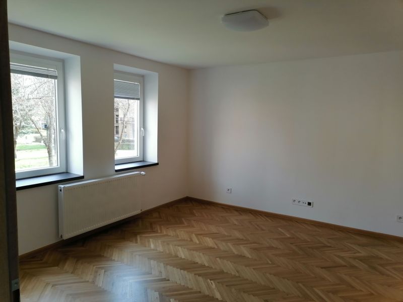 A spacious room with wooden decor flooring and large windows in a 2-room apartment.