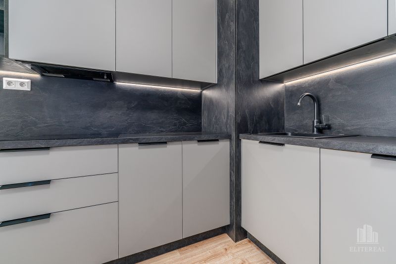 Dark gray kitchen unit with matte cabinets and a wooden decor floor in a 2-room apartment.