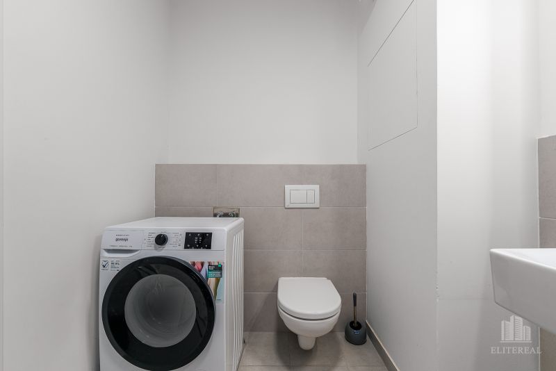 Bathroom with a washing machine and toilet in a 2-room apartment, light neutral wall colors.