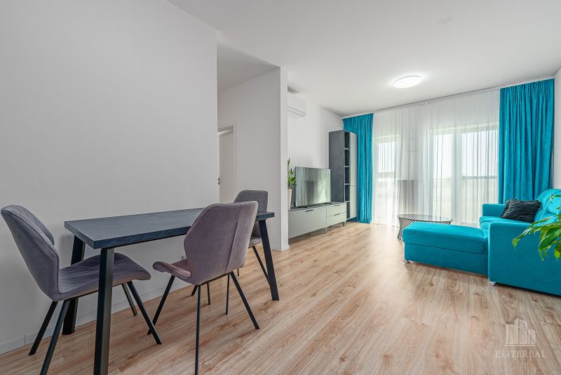A bright living room with wood-patterned flooring, a turquoise sofa, and a dining table.
