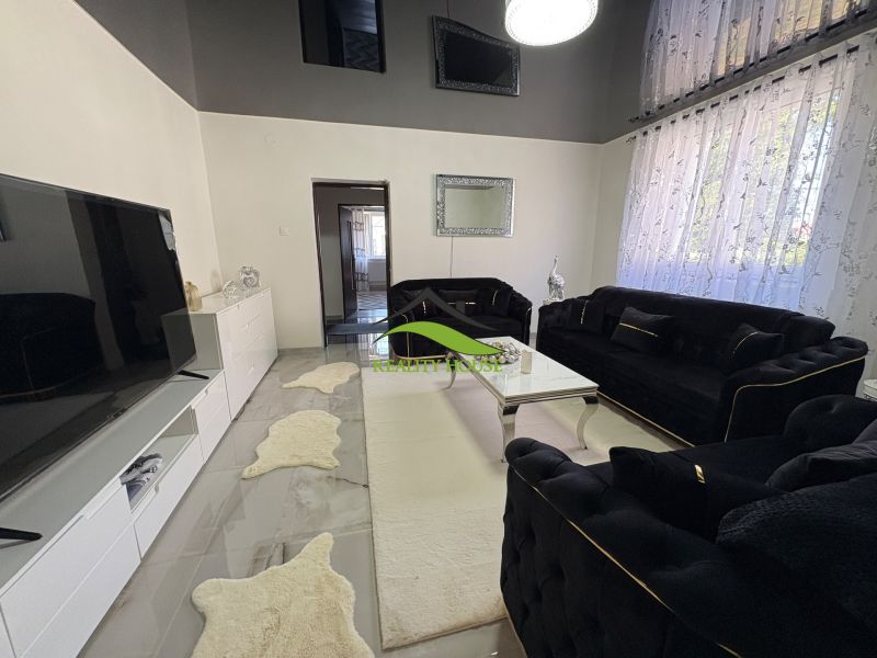 A living room in a family house with white furniture, a black sofa, and decorative rugs.