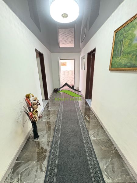 A hallway in a family house with a marble floor, a carpet, and a decorative vase.