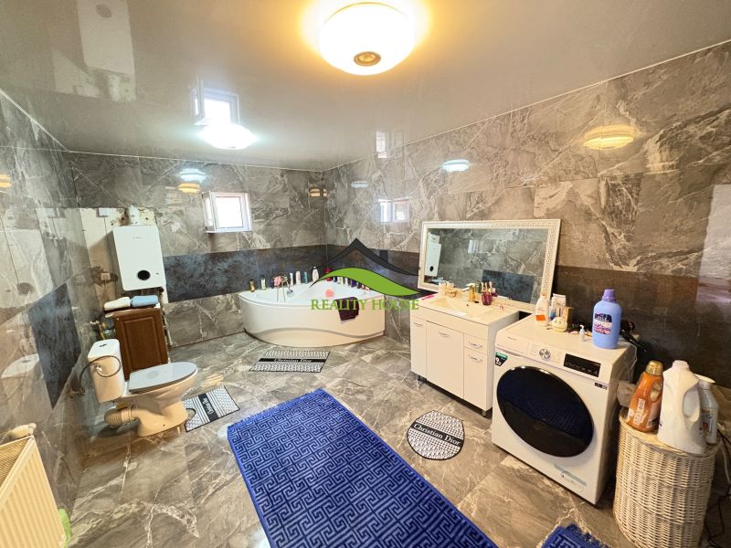 A bathroom in a family house with a bathtub, washing machine, and dark-colored tiles.
