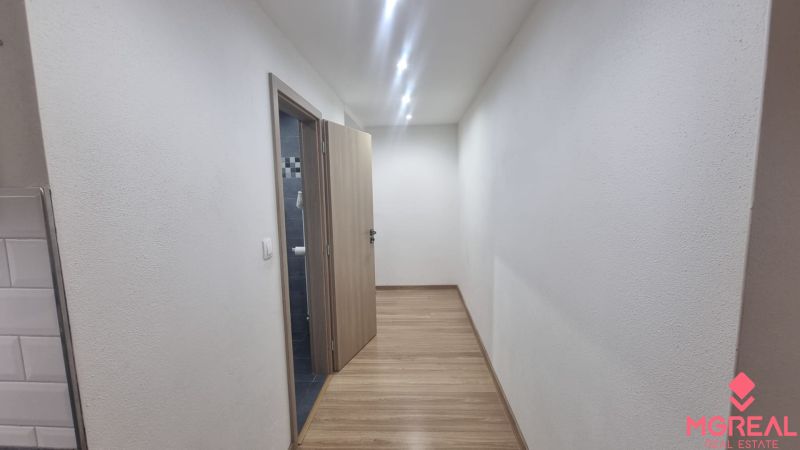 A hallway with bright lighting, a wooden decor floor, and a bathroom door.