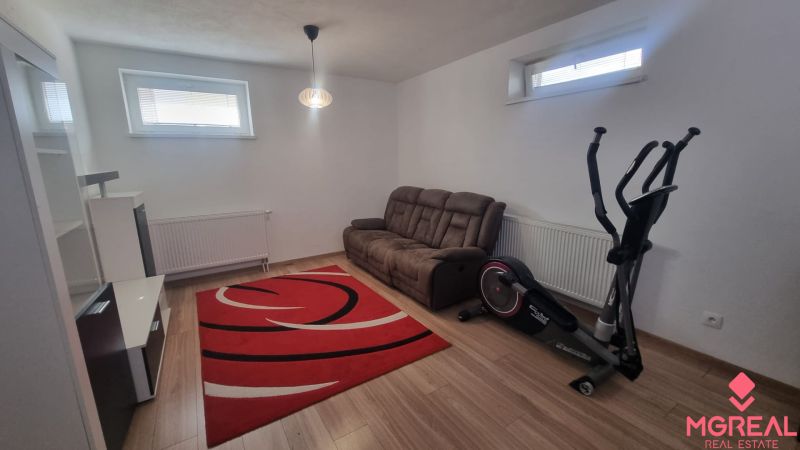 Living room in a two-room apartment with a sofa, exercise bike, and wooden decor flooring.