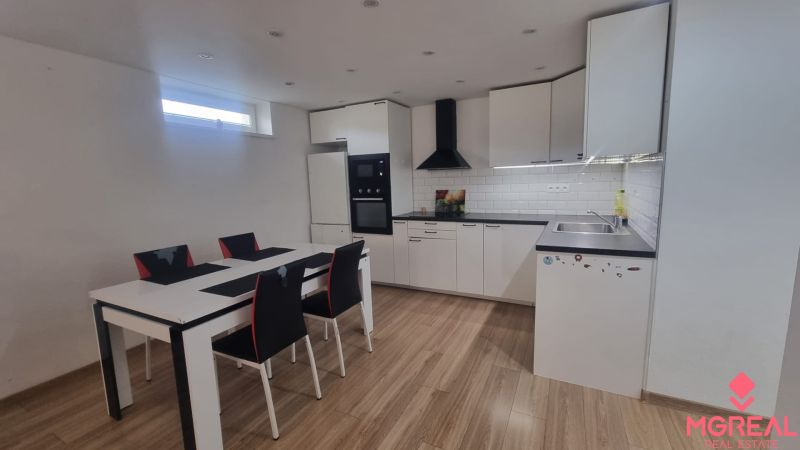 A kitchen in a 2-room apartment with white furniture, a dining table, and a floor with a wooden decor.