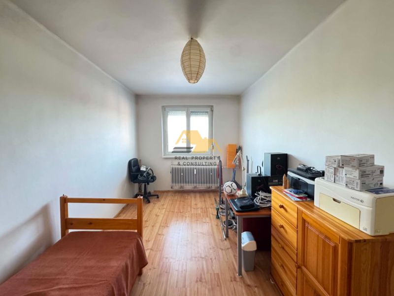 A room in a 3-room apartment with a wooden decor floor, simple furnishings, and a work corner.