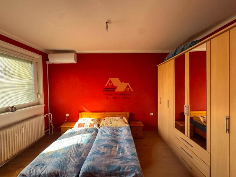 Bedroom with a red wall, wood-patterned flooring, wardrobe, and air conditioning in a 3-room apartment.