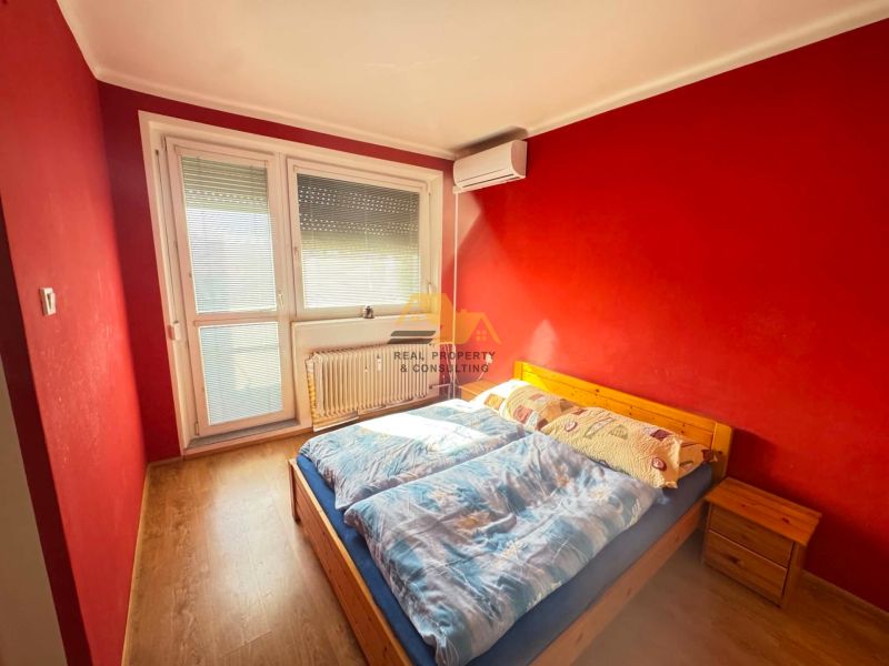 A bedroom with red walls, a wooden bed, and a floor with a wooden decor in a 3-room apartment.