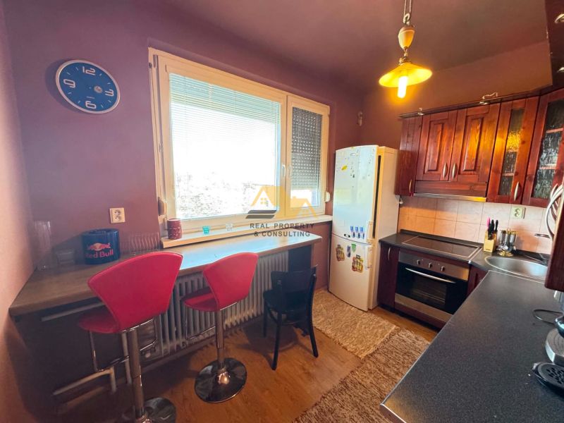 A kitchen in a 3-room apartment with bar stools and a wooden decor floor.