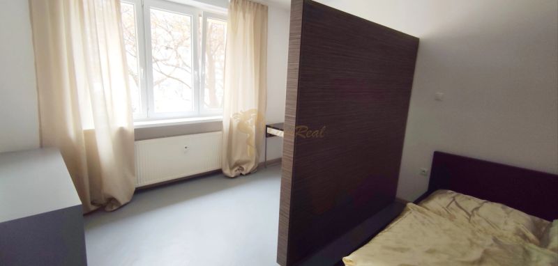 A bright bedroom in a two-room apartment with a window and curtains, a radiator, and a bed.