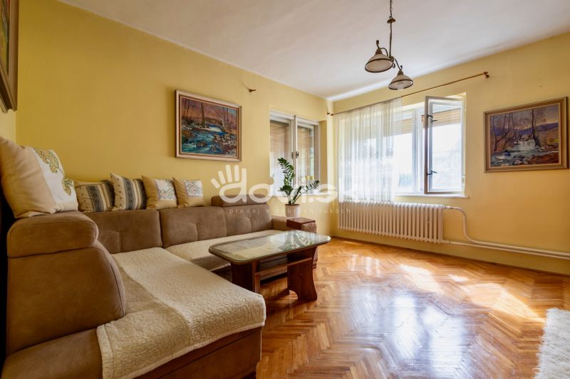 Living room in a family house with a sofa, paintings, and a wooden-patterned floor.