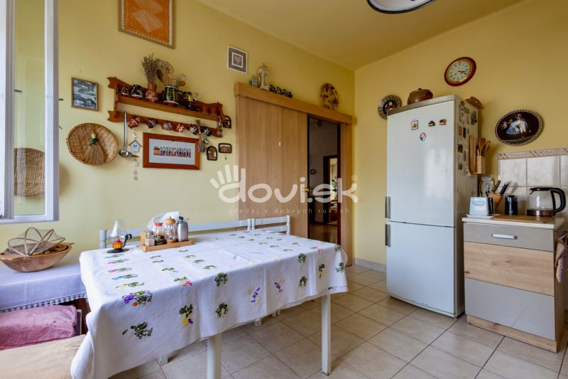 A kitchen in a family house with an embroidered tablecloth, a refrigerator, and decorations on the wall.