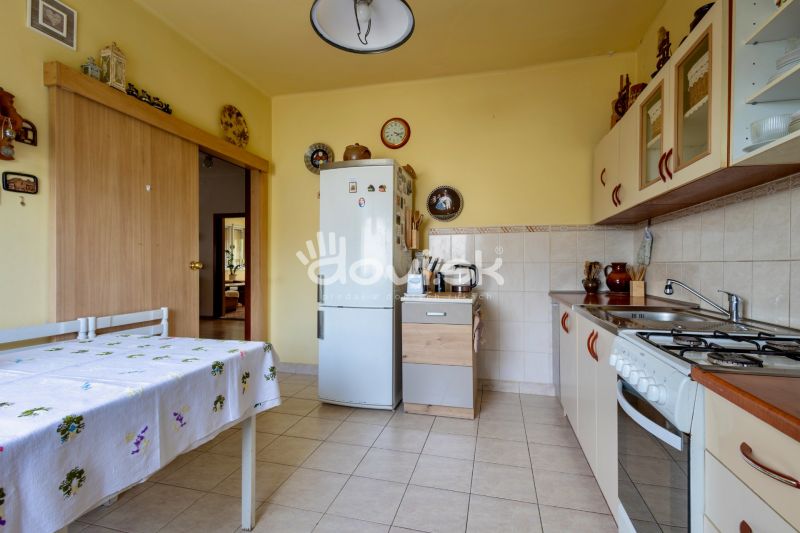 A kitchen in a family house with tiles, a refrigerator, and a table with a tablecloth.