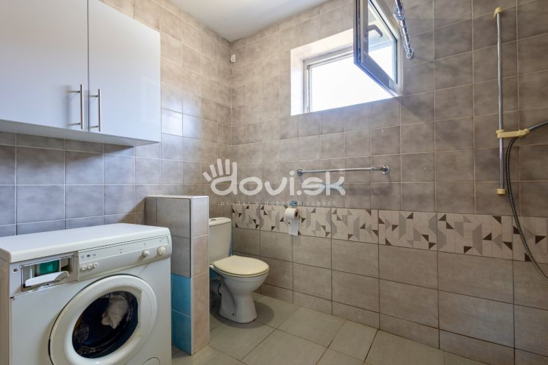 A bathroom in a family house with a washing machine, toilet, and tiles in neutral colors.