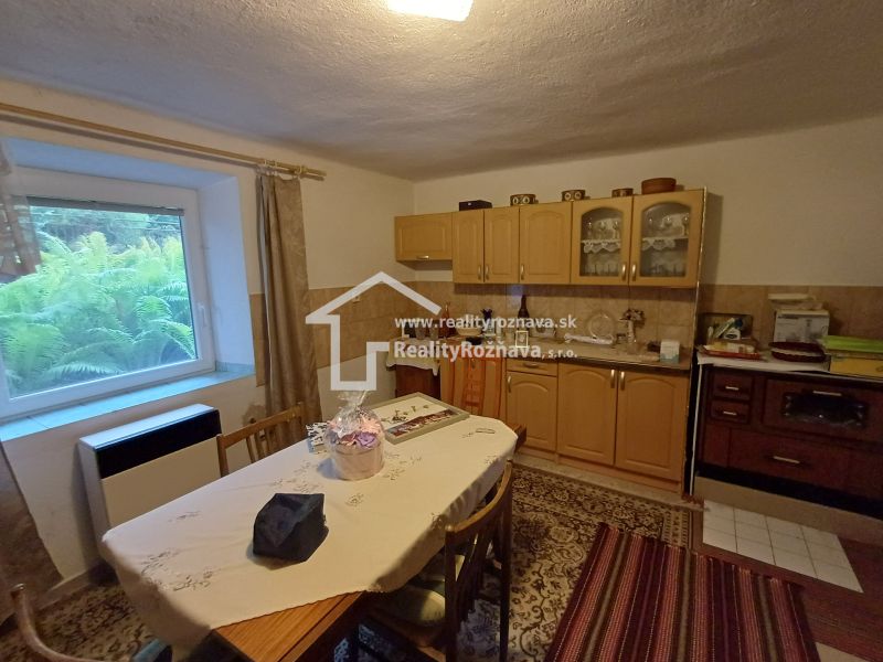 A kitchen in a family house with wooden cabinets, a large window, and a carpet on the floor.