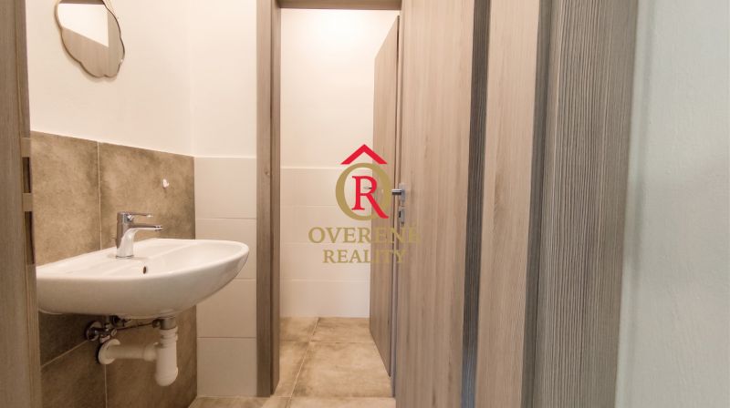 A bathroom in an office with a sink, mirror, and tiles with a wood decor.