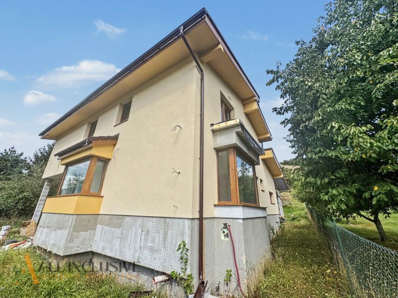 A family house in Veličná surrounded by trees and grass under a blue sky.