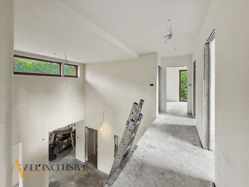 A spacious hallway in a family house with a view of the garden, white walls, and a ladder.