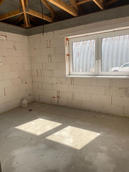 A room construction in a family house with an open wooden ceiling and a concrete floor.