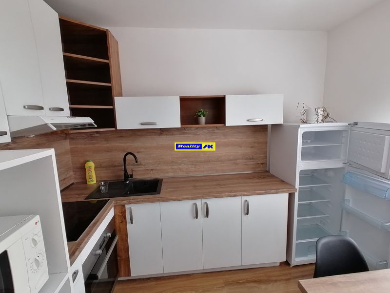 A kitchen in a studio apartment with a wooden decor floor and an open refrigerator.