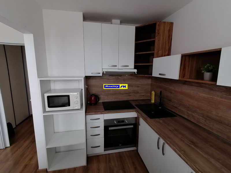 A kitchen with white cabinets and appliances in a studio apartment; floor with wood decor.