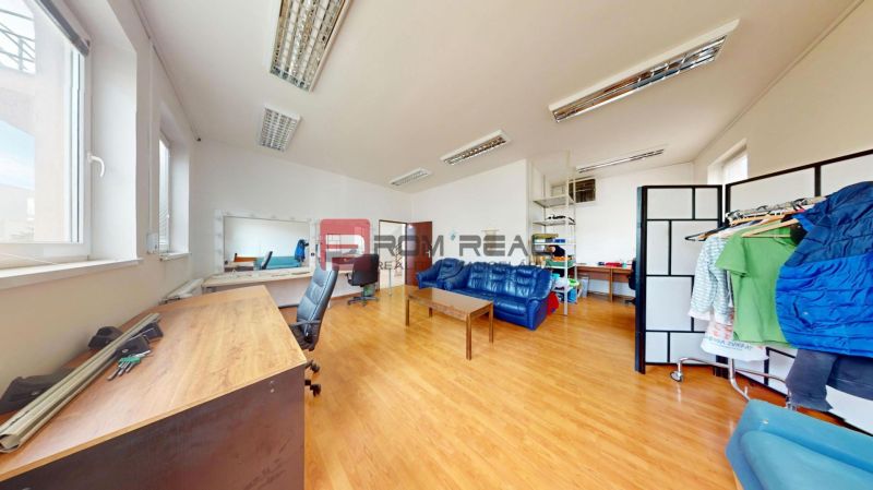 Interior of an office with wood-patterned flooring, a sofa, a desk, and a mirror.