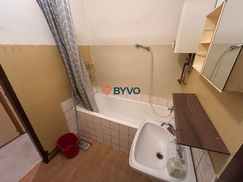 A bathroom in a 3-room apartment with a bathtub and a floor with a wooden decor.