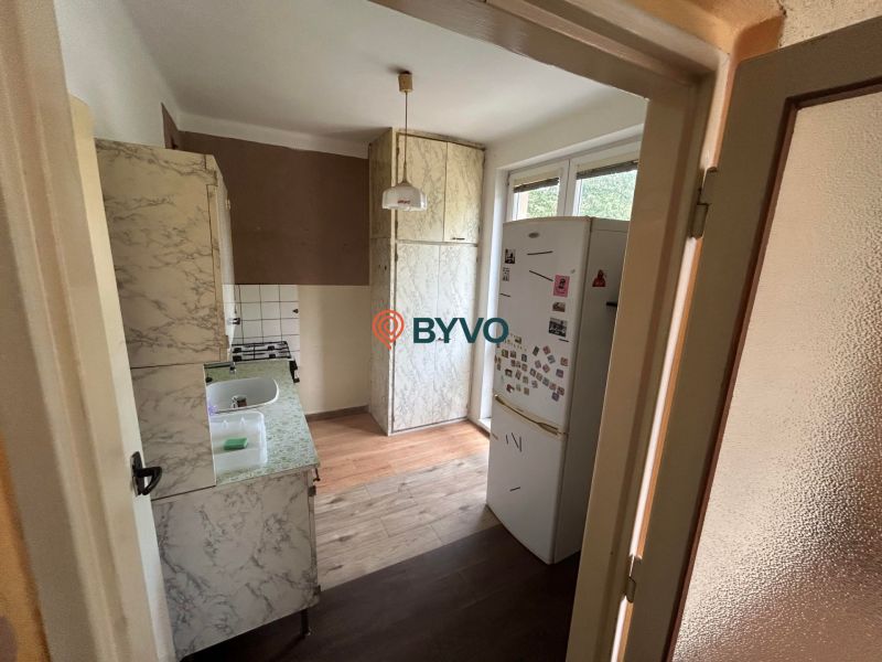 The kitchen of a three-room apartment with a wooden-patterned floor and a patterned kitchen unit.