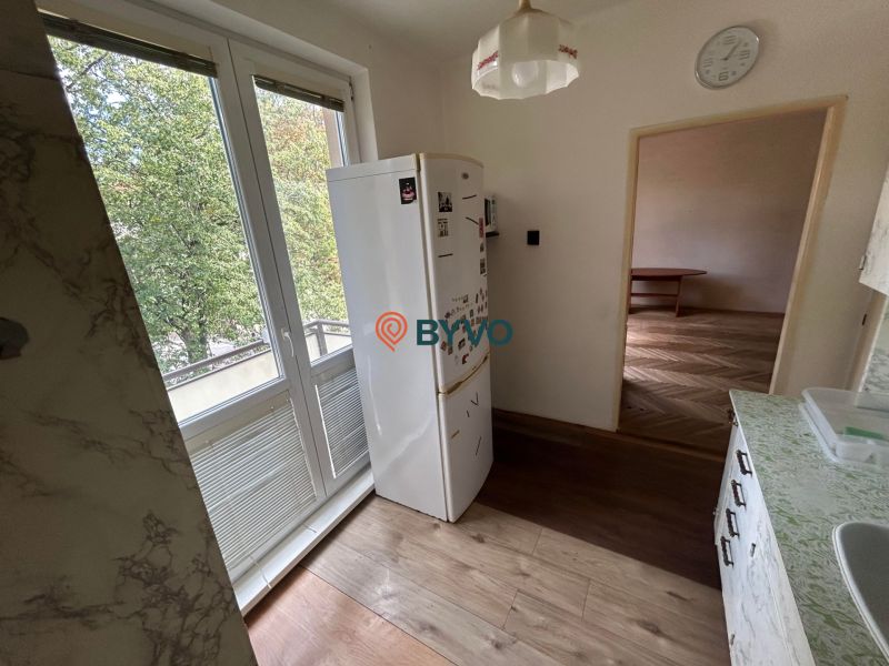 A kitchen with a wooden decor floor in a 3-room apartment, view of the trees.