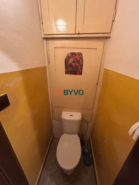 A toilet with a floral picture and a yellow wall in a 3-room apartment.