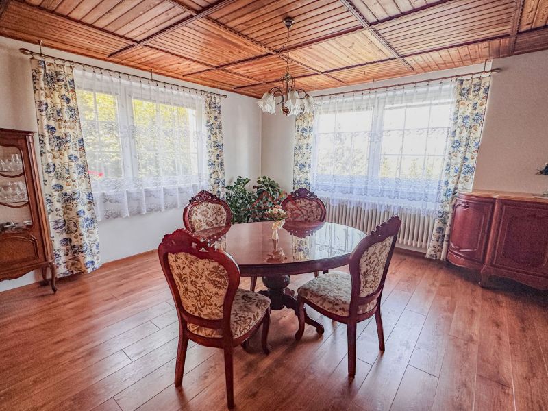 A dining room with a wooden ceiling, a floor with a wooden decor, and antique furniture.