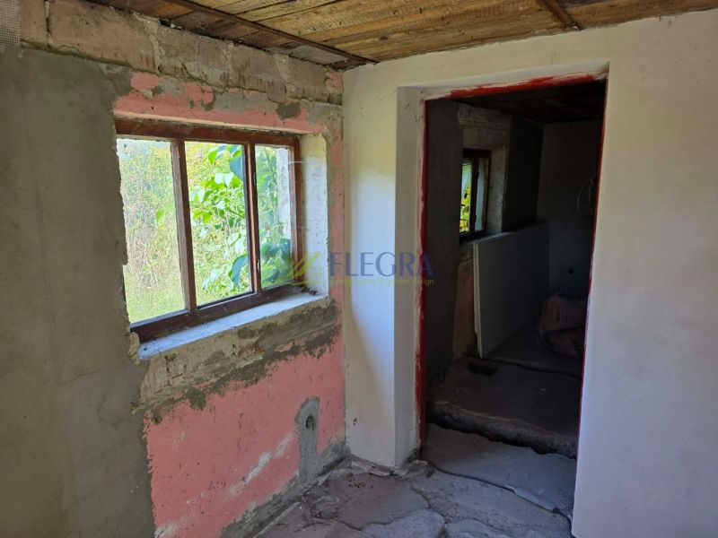 The interior of a cottage with peeling plaster and a view of the garden through the window.