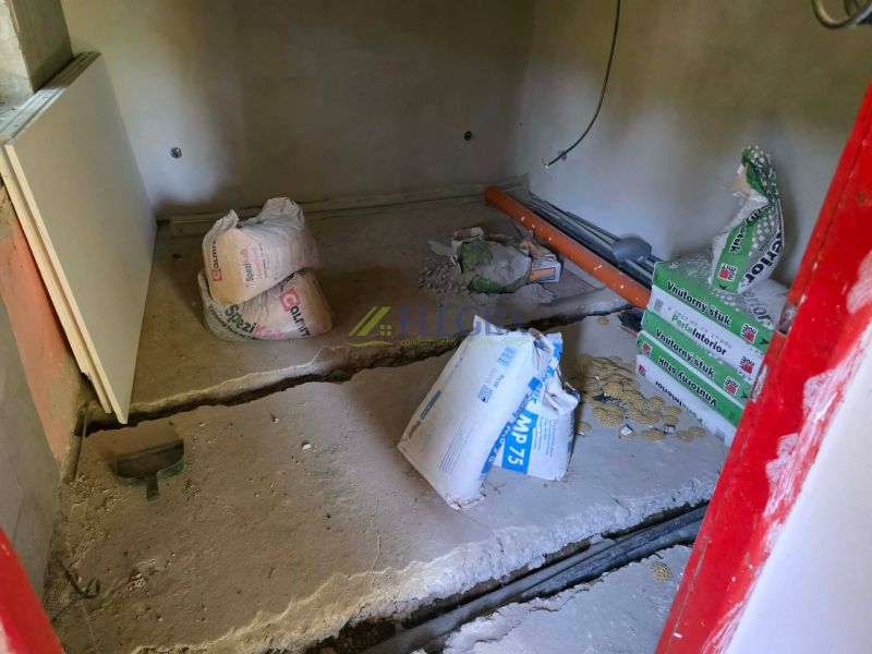 A cottage under reconstruction with materials on a concrete floor, ready for construction work.