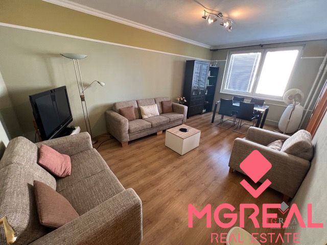 Living room with wood-patterned flooring, sofas, and a coffee table in a three-room apartment.